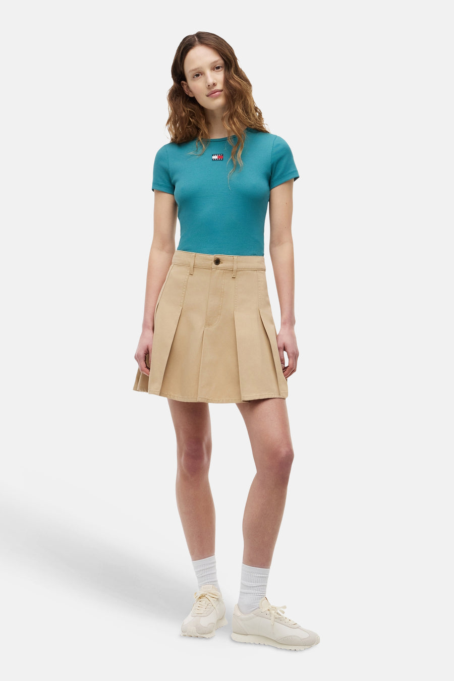 TOMMY JEANS ribfluwelen T-shirt in groenblauw met logo op de borst, gecombineerd met een beige plooirok.