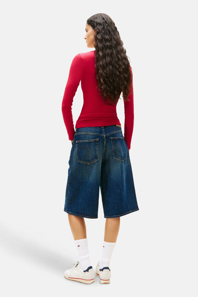 Roze T-shirt met lange mouwen van TOMMY JEANS, gedragen met een wijde spijkerbroekshort en witte sneakers.