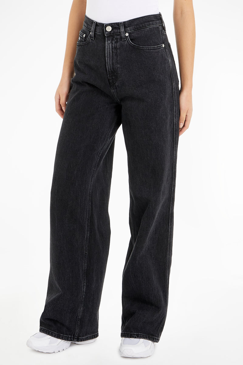 Jeans larges noirs en denim de Tommy Jeans, coupe ample et chaussures blanches apparentes.
