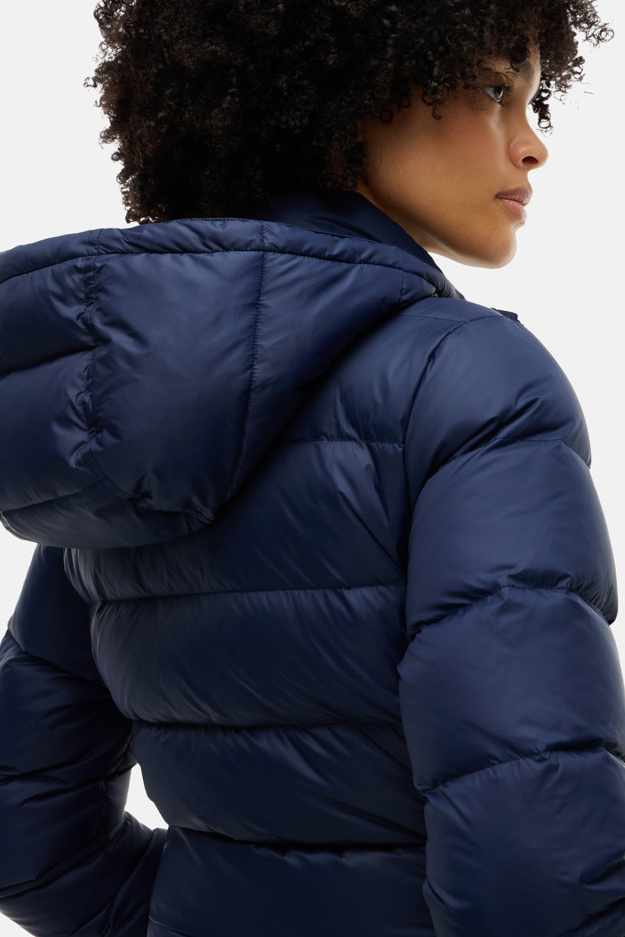 Navy blue quilted puffer jacket with hood, side view of model, shiny nylon material, structured stitching, cropped fit