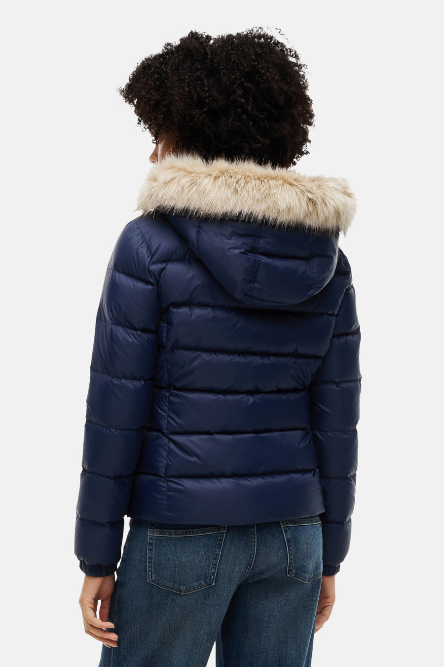 Navy blue quilted puffer jacket with faux fur hood trim, back view, worn with dark denim jeans