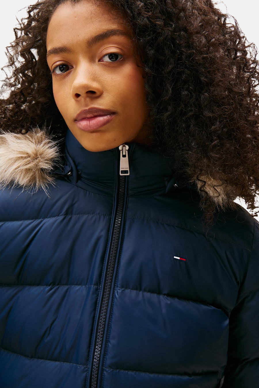 Navy blue quilted puffer jacket with fur-trimmed hood by Tommy Jeans, front zip closure, chest flag logo, close-up view