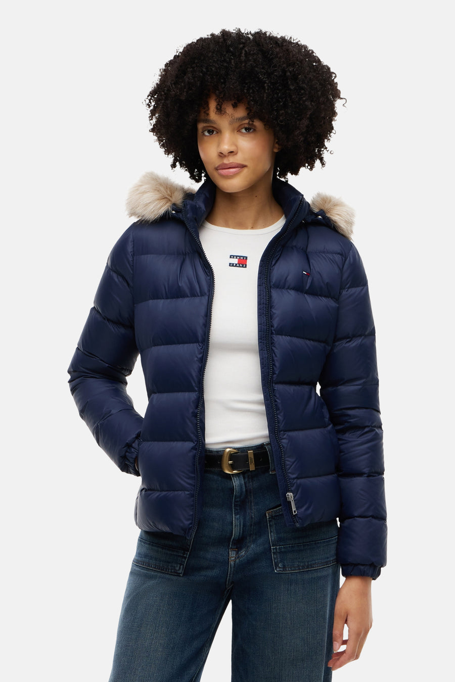 Navy blue quilted puffer jacket with fur-trimmed hood by Tommy Jeans, worn over white top and jeans, front view
