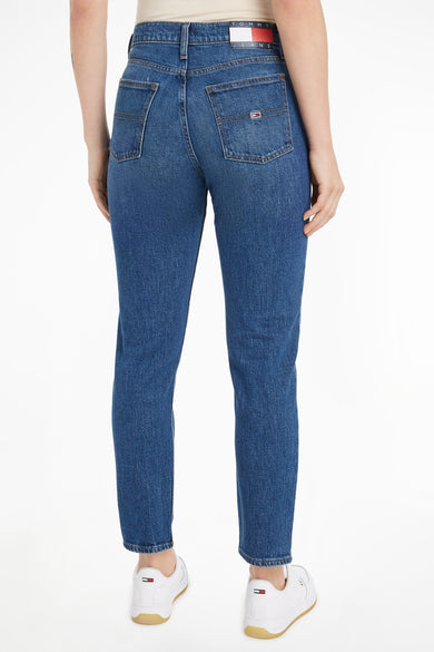 Jeans slim en denim bleu foncé de Tommy Jeans avec poches arrières et logo sur les chaussures blanches.
