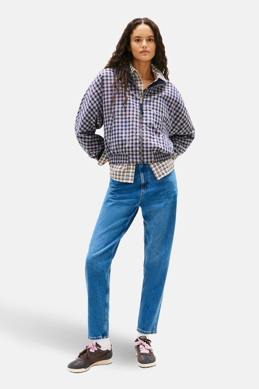 Jean mom bleu moyen de TOMMY JEANS, porté avec une veste à carreaux et des baskets marron.
