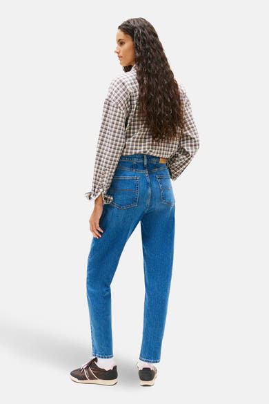 Jean Mom en denim bleu moyen de TOMMY JEANS, avec une chemise à carreaux et des baskets marron et rose.
