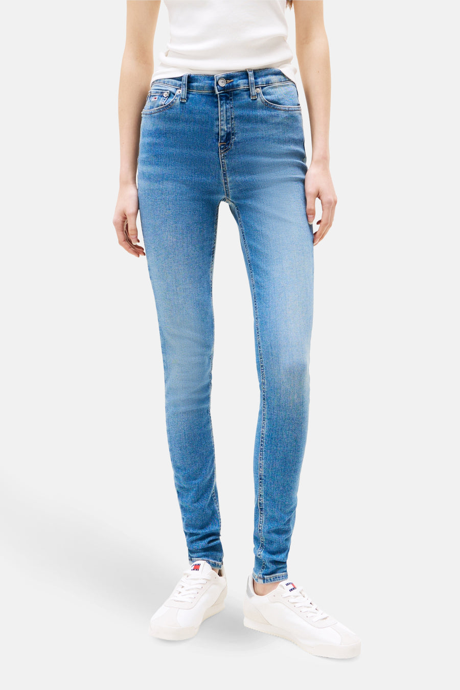 Jean skinny bleu moyen de Tommy Jeans, porté avec un t-shirt blanc et des baskets blanches.
