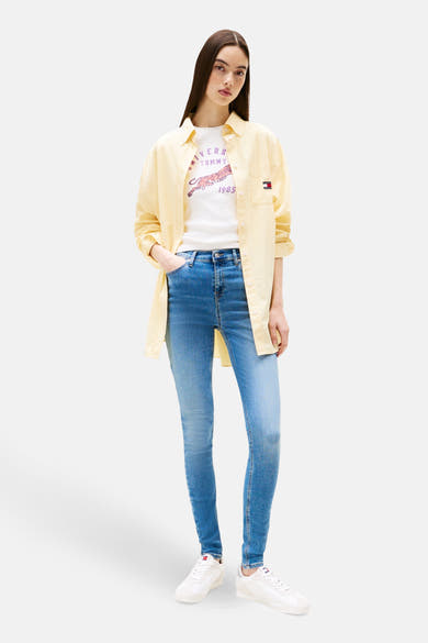 Jean skinny bleu moyen de Tommy Jeans, porté avec une chemise jaune clair et un T-shirt imprimé.