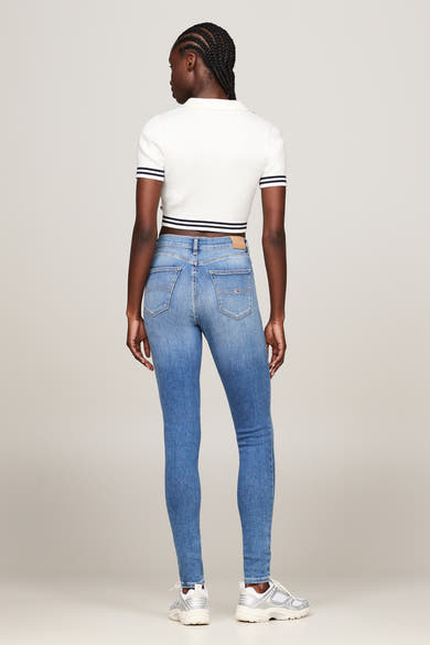 Middelblauwe skinny jeans van TOMMY JEANS, gedragen met een witte geribbelde top en witte sneakers.