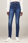Jean skinny en denim bleu foncé de TOMMY JEANS, porté avec un pull blanc et des baskets blanches.
