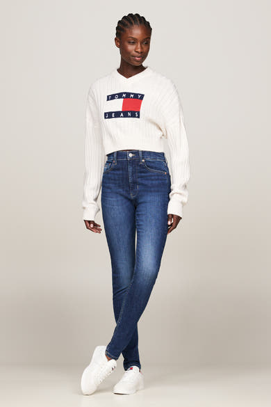 Jean skinny bleu foncé de TOMMY JEANS, porté avec un pull en maille côtelée et des baskets blanches.
