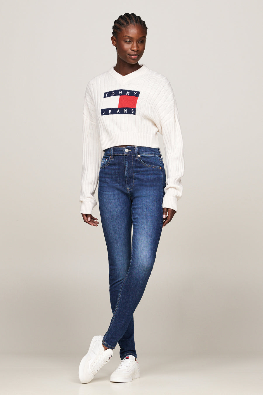 Jean skinny bleu foncé de TOMMY JEANS, porté avec un pull en maille côtelée et des baskets blanches.