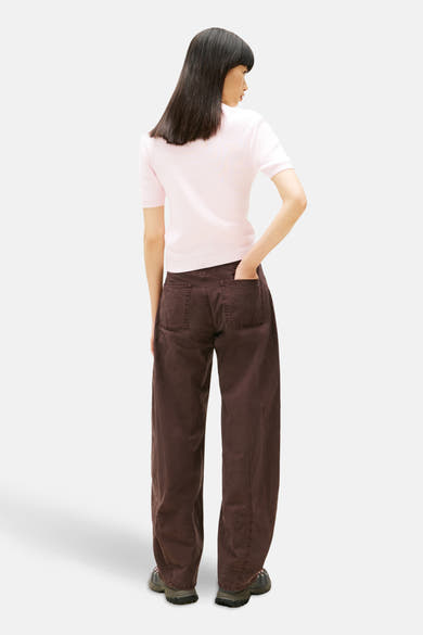 Pull à col rond rose de Tommy Jeans, porté avec un pantalon ample marron et des chaussures de randonnée.