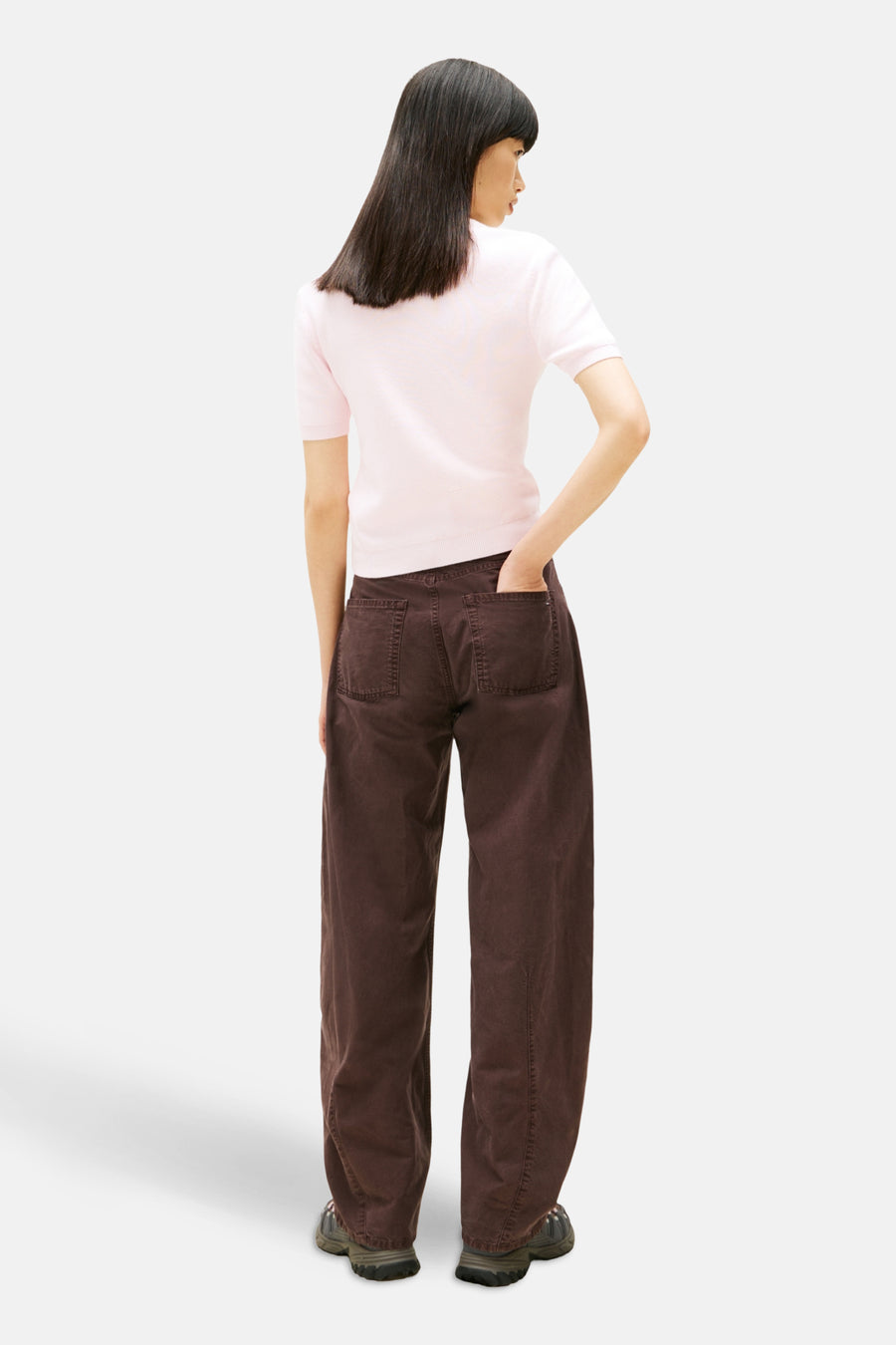 Pull à col rond rose de Tommy Jeans, porté avec un pantalon ample marron et des chaussures de randonnée.