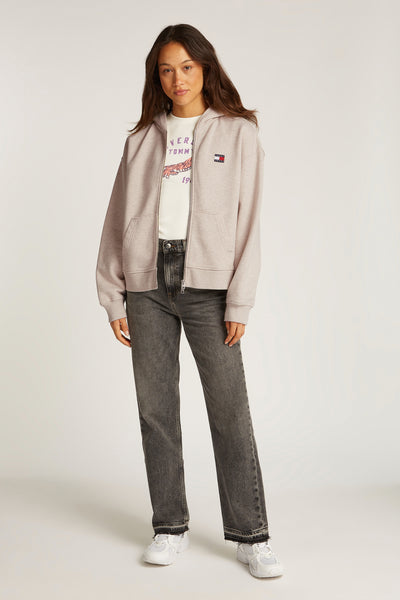 Polaire beige de TOMMY JEANS avec fermeture éclair, porté sur un t-shirt imprimé et un jean gris.