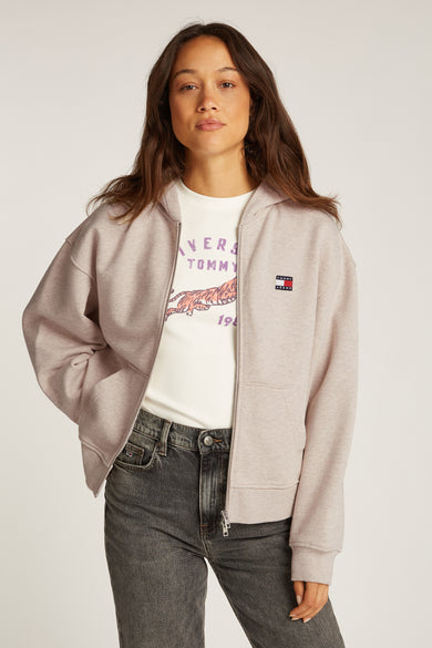 Polaire beige de TOMMY JEANS, avec fermeture éclair, poches et porté avec un t-shirt imprimé et un jean gris.