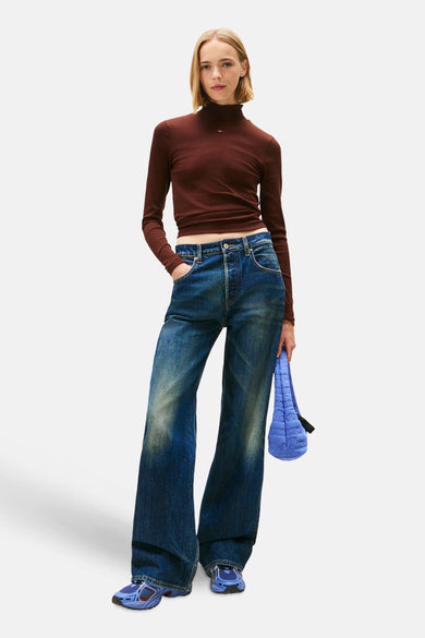 Bruin T-shirt met lange mouwen van Tommy Jeans, gedragen met een wijde jeans en blauwe sneakers.