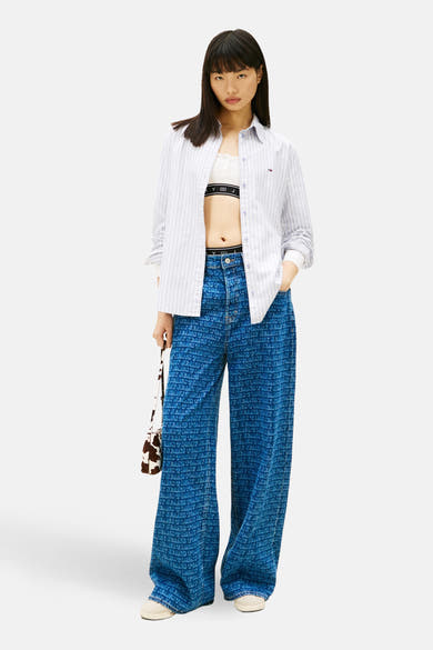 Blauw gestreept overhemd met lange mouwen van TOMMY JEANS, open gedragen over een witte top, met een bedrukte jeans.