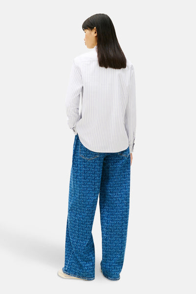Chemise à manches longues bleue à rayures, de TOMMY JEANS, portée avec un pantalon imprimé logo.
