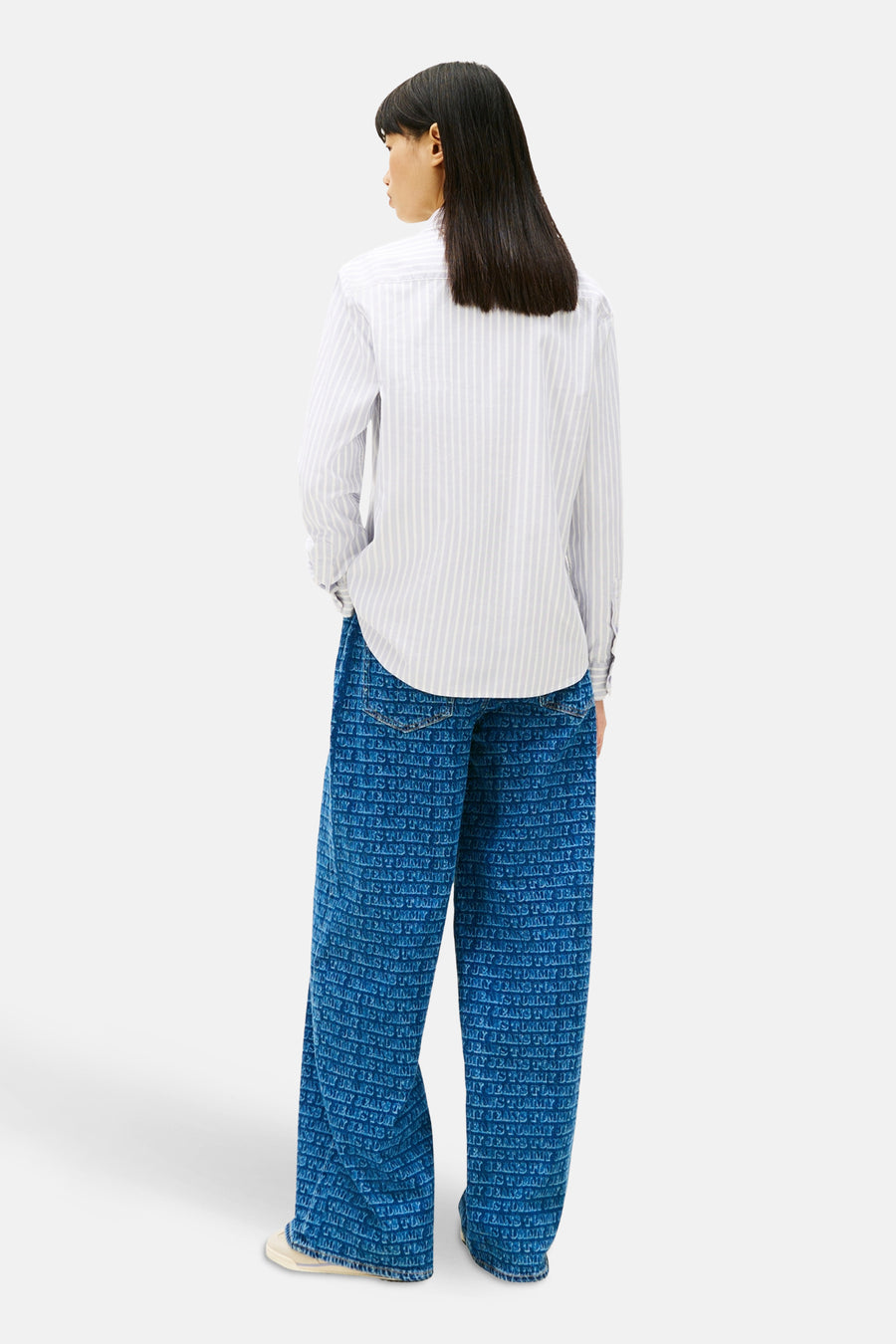 Chemise à manches longues bleue à rayures, de TOMMY JEANS, portée avec un pantalon imprimé logo.
