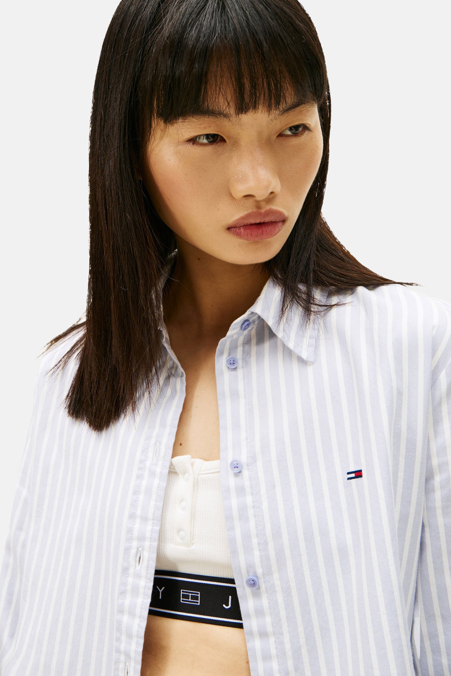 Blauwe gestreepte blouse met lange mouwen van TOMMY JEANS, gedragen open over een witte tanktop en een logoband.