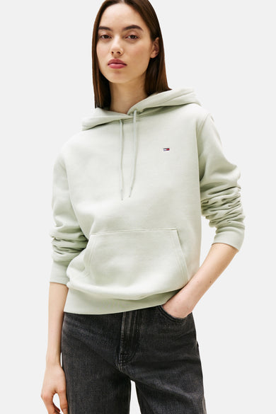 Groene sweater van TOMMY JEANS, met capuchon, kangoeroezak en gedragen met een zwarte jeans.
