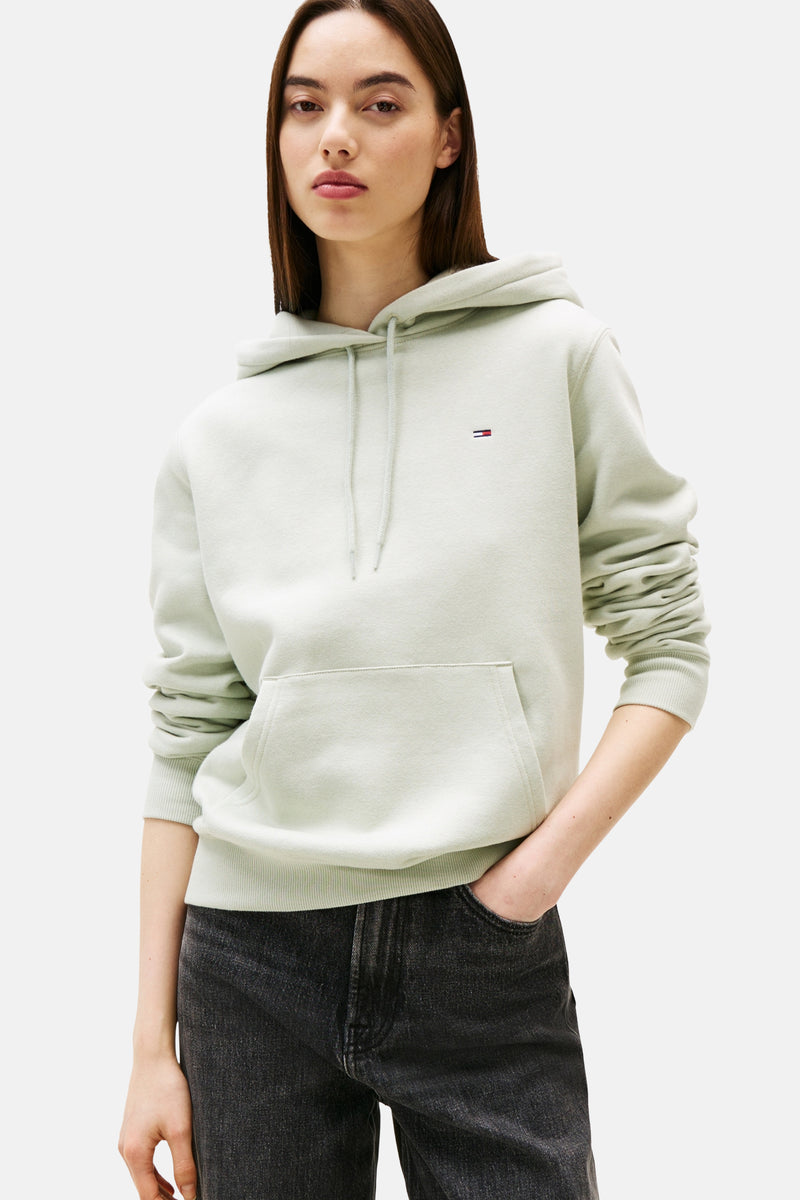 Groene sweater van TOMMY JEANS, met capuchon, kangoeroezak en gedragen met een zwarte jeans.