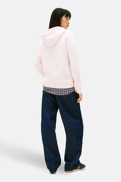 Sweat-shirt rose avec capuche de TOMMY JEANS, porté avec une chemise à carreaux et un jean large, vue de dos.