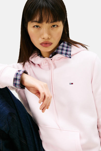 Sweat rose à capuche de Tommy Jeans, porté sur une chemise à carreaux, et un jean foncé.