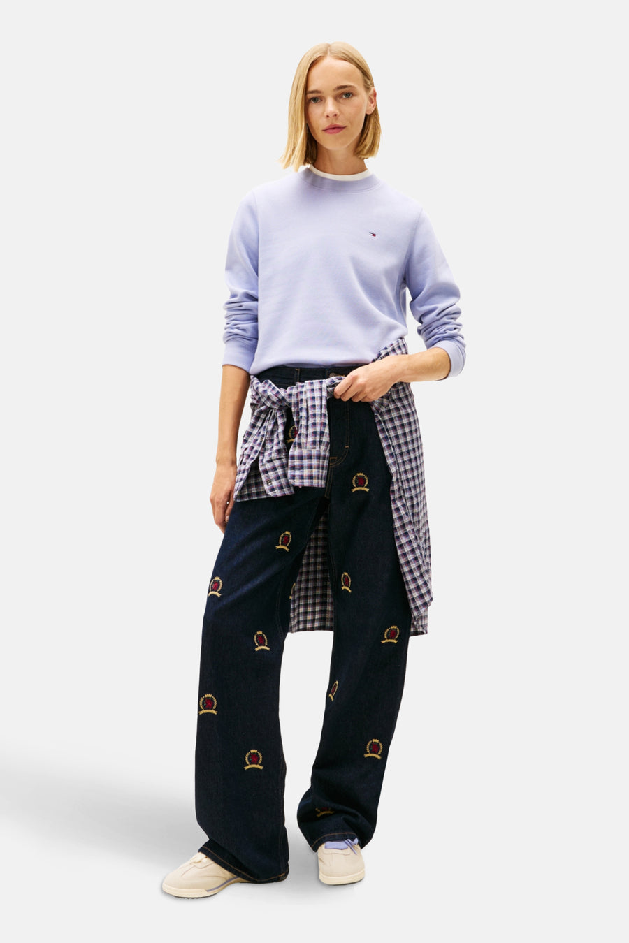 Paarse TOMMY JEANS sweater met een wit T-shirt eronder, gedragen met een geruit overhemd om de taille geknoopt en een geborduurde jeans.