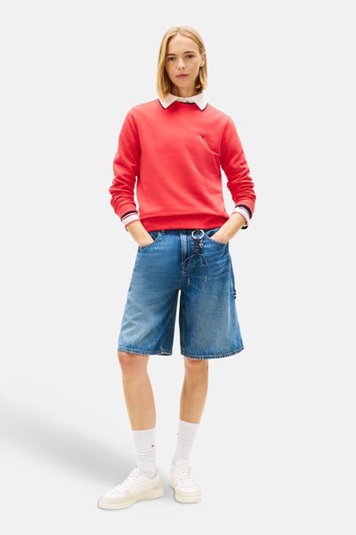 Sweat rouge de TOMMY JEANS, porté avec un col blanc, des shorts en jean et des baskets blanches.
