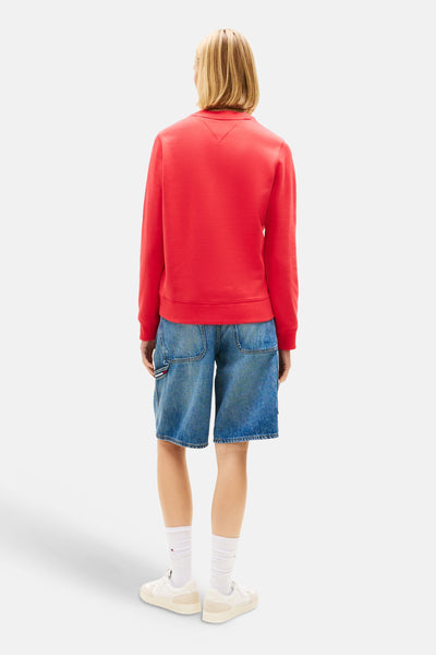 Rode sweatshirt van TOMMY JEANS, met een ronde hals, gedragen met een spijkerbroekshort en witte sneakers.