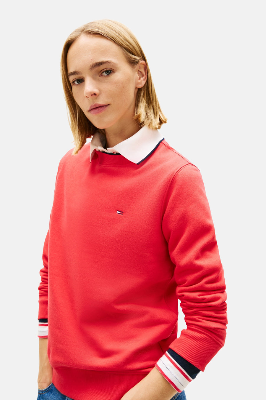 Sweat col O rouge de TOMMY JEANS, porté sur une chemise à col blanc et poignets rayés.