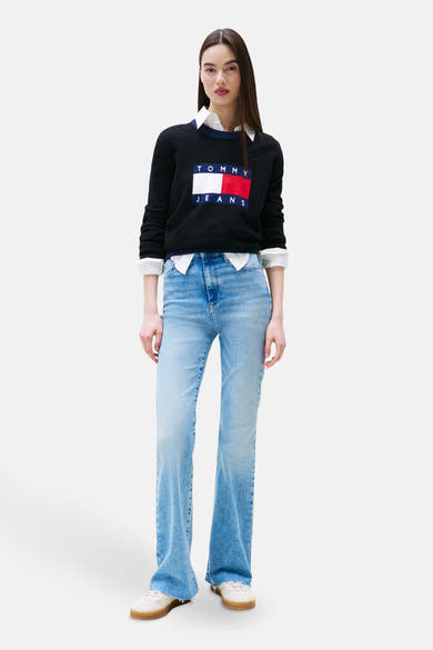 Wijde spijkerbroek in lichtblauw denim van TOMMY JEANS gedragen met een zwarte trui met logo en een wit overhemd.