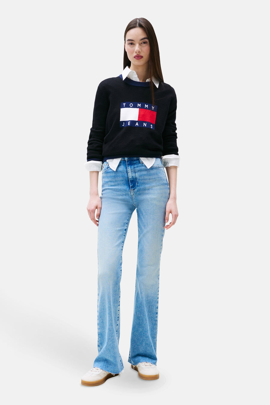 Wijde spijkerbroek in lichtblauw denim van TOMMY JEANS gedragen met een zwarte trui met logo en een wit overhemd.