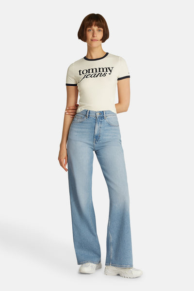 Jean large en denim bleu clair de TOMMY JEANS, porté avec un t-shirt crème à bordure noire et des baskets blanches.