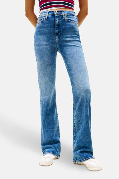 Uitlopende jeans in middinblauw denim van TOMMY JEANS, gedragen met een gestreept rood en marineblauw topje en een marineblauw jasje.