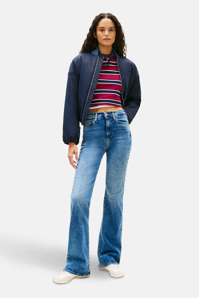 Jean évasé en denim bleu moyen de TOMMY JEANS, porté avec un haut rayé rouge et bleu marine et une veste bleu marine.