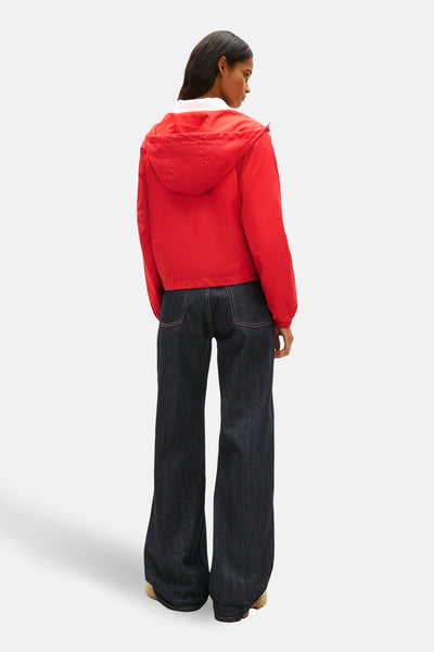Veste courte rouge de TOMMY JEANS, avec capuche et ourlet élastiqué, portée avec un pantalon évasé en denim foncé.