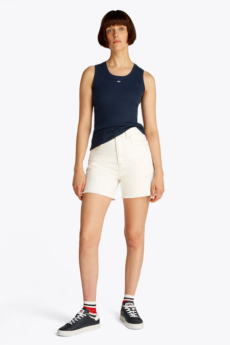 Débardeur bleu uni de Tommy Jeans, porté avec un short blanc taille haute et des baskets noires.