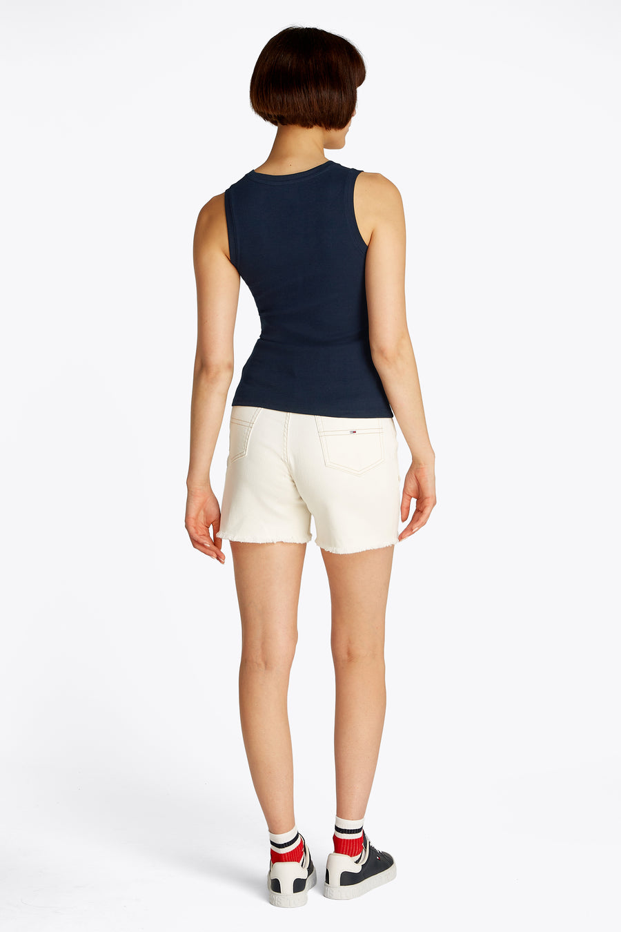 Top uni bleu à manches courtes de Tommy Jeans, porté avec un short blanc en denim effiloché.