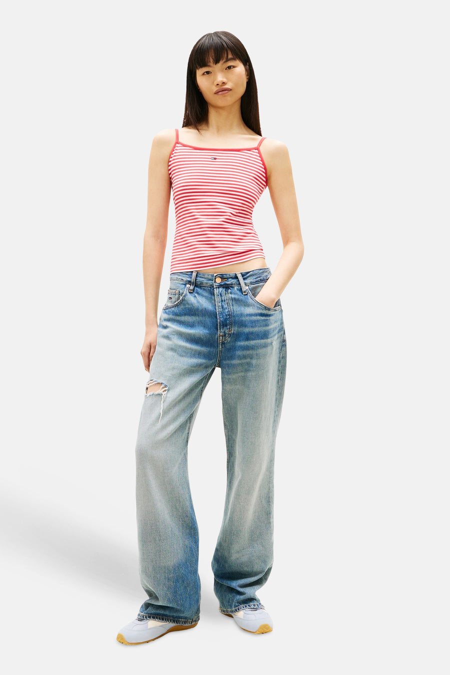 Débardeur multicolore par TOMMY JEANS, à rayures rouges et blanches, porté avec un jean ample déchiré.
