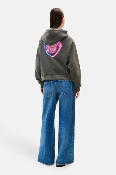 Grijze hoodie van TOMMY JEANS, met een lichtgevende print op de rug, gedragen met een wijde blauwe jeans.