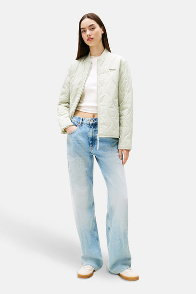 Korte groene jas van TOMMY JEANS met doorgestikt patroon, gedragen met een wijde jeans en een wit T-shirt.