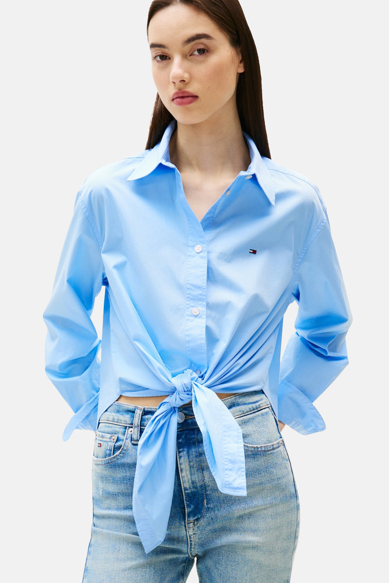 Blauwe blouse met lange mouwen van Tommy Jeans, geknoopt in de taille over een verbleekte spijkerbroek.