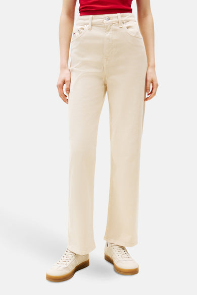 Beige kleurige broek van TOMMY JEANS, rechte pasvorm, gedragen met een rood T-shirt en witte sneakers.
