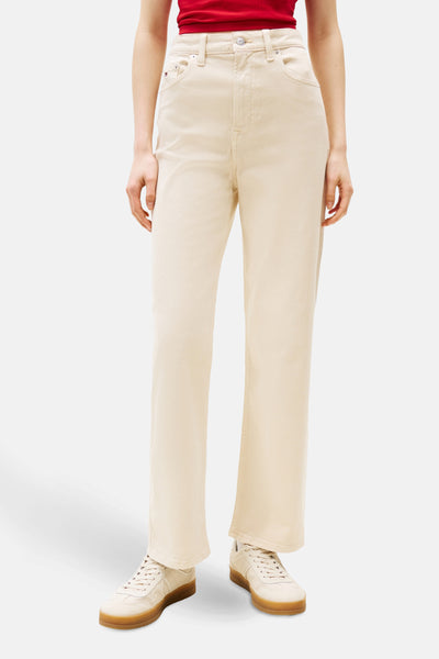 Pantalon coloré beige de TOMMY JEANS avec une coupe droite, porté avec un t-shirt rouge et des baskets crème.