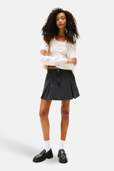 Zwarte korte rok van TOMMY JEANS met plooien, gedragen met een gestreept T-shirt en loafers.