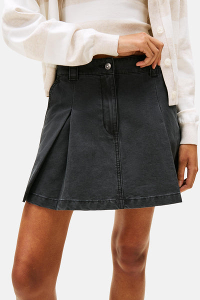 Jupe courte noire de TOMMY JEANS, avec plis et taille haute, portée avec un cardigan rayé clair.