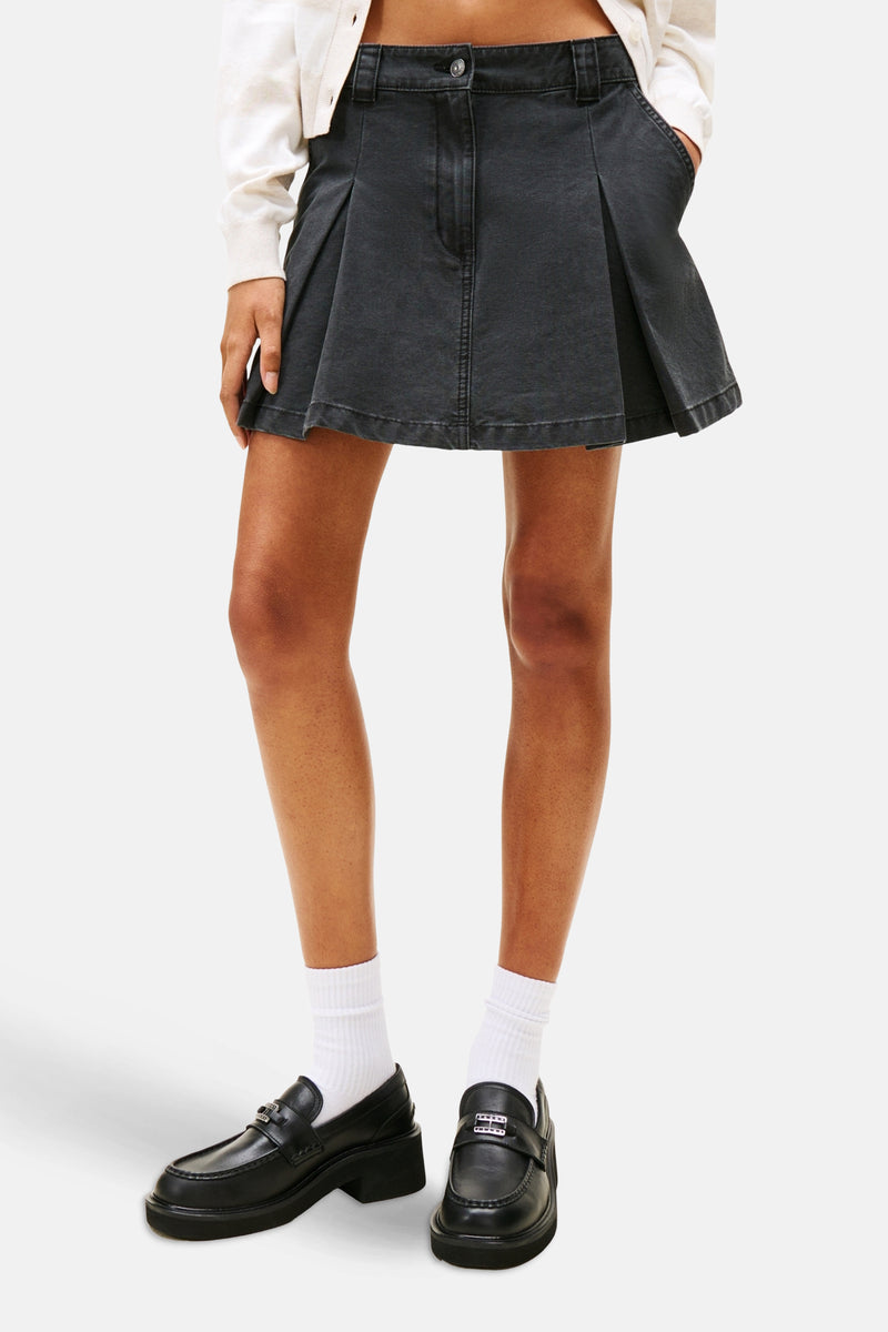 Zwarte korte geplooide rok van TOMMY JEANS, gedragen met witte sokken en zwarte loafers.